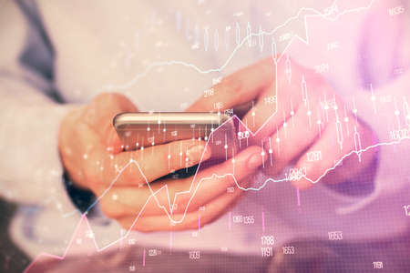 Double exposure of mans hands holding and using a digital device and forex graph drawing. Financial...