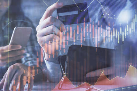 Double exposure of man and woman on-line shopping holding a credit card and forex graph hologram...