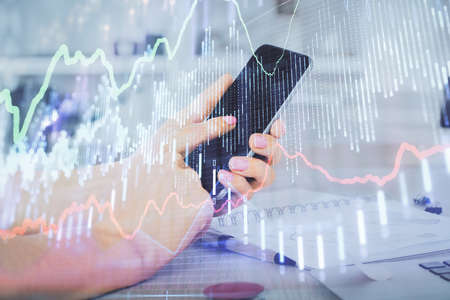 Double exposure of mans hands holding and using a digital device and forex graph drawing. Financial...
