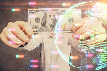 Double exposure of world map drawing hologram and us dollars bills and man hands.