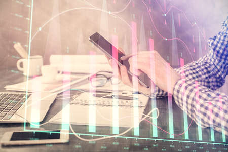Double exposure of mans hands holding and using a digital device and forex graph drawing. Financial...
