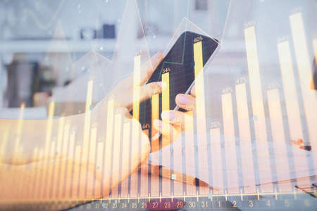 Double exposure of mans hands holding and using a digital device and forex graph drawing. Financial...