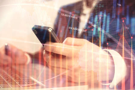 Multi exposure of mans hands holding and using a digital phone and forex graph drawing. Financial...