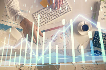 Multi exposure of mans hands typing over computer keyboard and forex graph hologram drawing. Top...