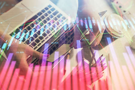 Double exposure of businesswoman hands typing on computer and financial graph hologram drawing....