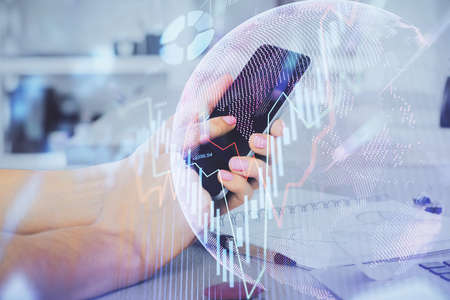 Double exposure of mans hands holding and using a digital device and forex graph drawing. Financial...