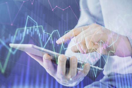Double exposure of mans hands holding and using a digital device and forex graph drawing. Financial...
