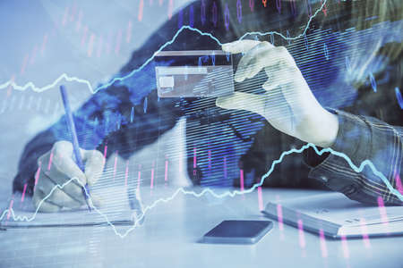 Double exposure of woman on-line shopping holding a credit card and financial graph drawing. Stock...