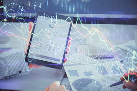 Double exposure of mans hands holding and using a digital device and forex graph drawing. Financial...