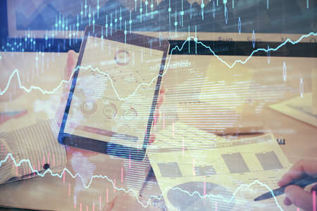 Double exposure of mans hands holding and using a digital device and forex graph drawing. Financial...