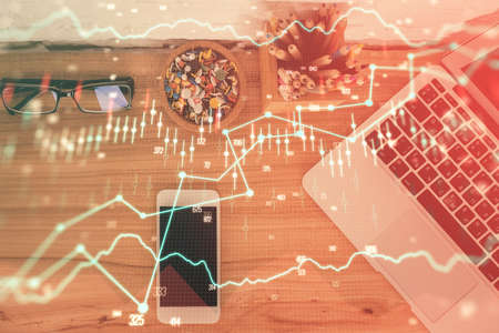 Double exposure of financial graph hologram over desktop with phone. Top view. Mobile trade platform...