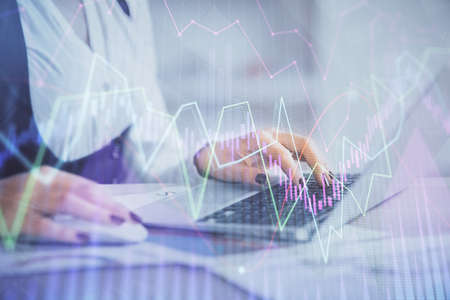 Double exposure of businesswoman hands typing on computer and forex graph hologram drawing....