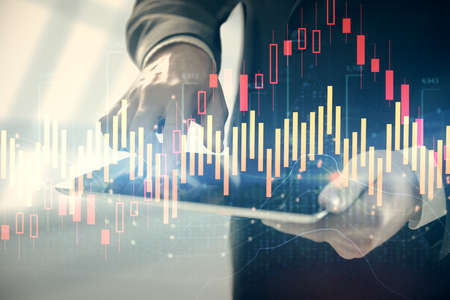 Double exposure of mans hands holding and using a digital device and forex graph drawing. Financial...