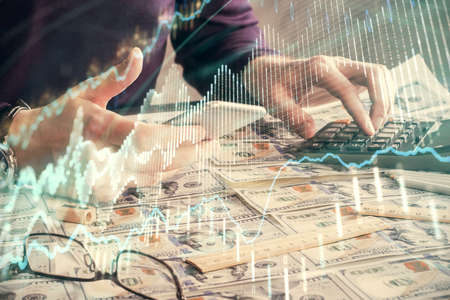 Double exposure of mans hands holding and using a digital device and forex graph drawing. Financial...