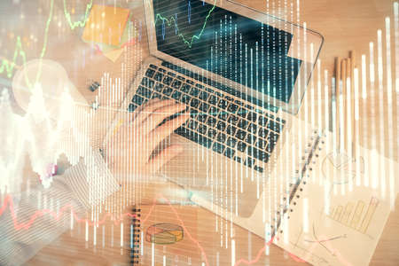 Double exposure of mans hands typing over computer keyboard and forex graph hologram drawing. Top...