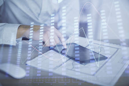 Double exposure of mans hands holding and using a digital device and forex graph drawing. Financial...