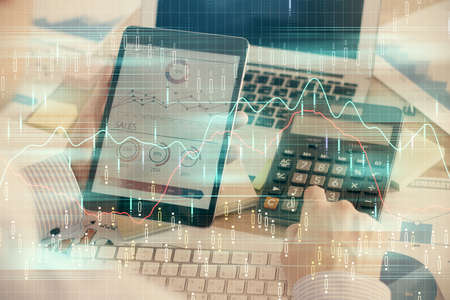 Double exposure of mans hands holding and using a digital device and forex graph drawing. Financial...