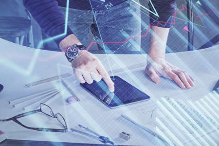 Double exposure of mans hands holding and using a digital device and forex graph drawing. Financial...