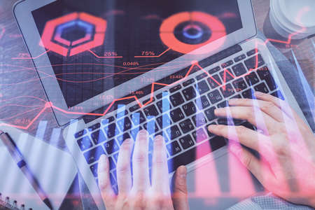 Double exposure of mans hands typing over computer keyboard and forex graph hologram drawing. Top...