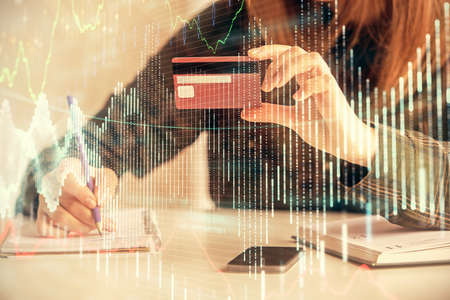 Double exposure of woman on-line shopping holding a credit card and financial graph drawing. Stock...