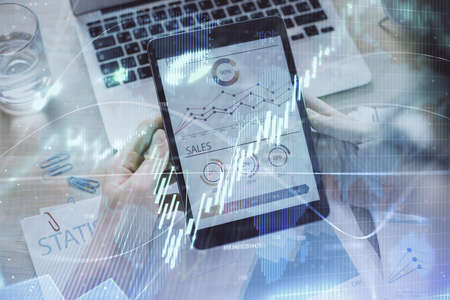Double exposure of mans hands holding and using a digital device and forex graph drawing. Financial...