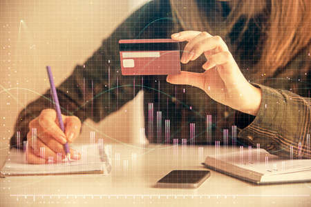 Double exposure of woman on-line shopping holding a credit card and financial graph drawing. Stock...