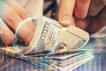 Double exposure of world map drawing hologram and us dollars bills and man hands.