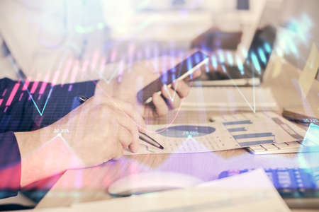 Double exposure of mans hands holding and using a digital device and forex graph drawing. Financial...
