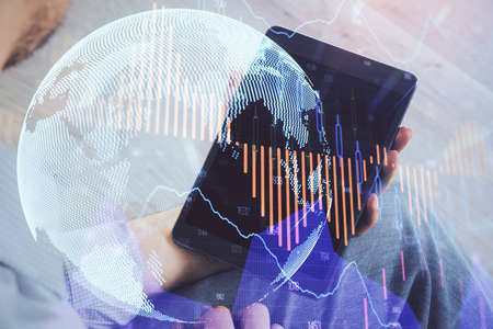 Double exposure of mans hands holding and using a digital device and forex graph drawing. Financial...