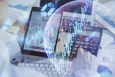 Double exposure of mans hands holding and using a digital device and forex graph drawing. Financial...