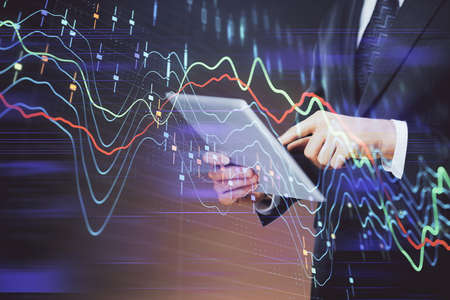 Double exposure of mans hands holding and using a digital device and forex graph drawing. Financial...