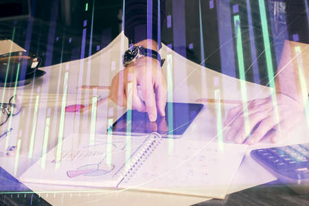 Double exposure of mans hands holding and using a digital device and forex graph drawing. Financial...