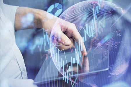 Double exposure of mans hands holding and using a digital device and forex graph drawing. Financial...