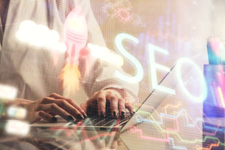 Double exposure of woman hands working on computer and seo hologram drawing. internet search concept.の写真素材