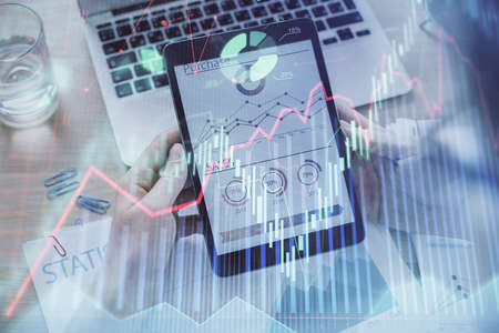 Double exposure of mans hands holding and using a digital device and forex graph drawing. Financial...