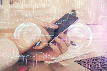 Double exposure of mans hands holding and using a digital device and forex graph drawing. Financial...