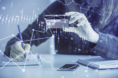 Double exposure of woman on-line shopping holding a credit card and financial graph drawing. Stock...