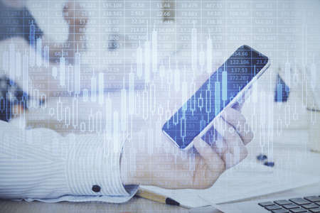 Double exposure of mans hands holding and using a digital device and forex graph drawing. Financial...