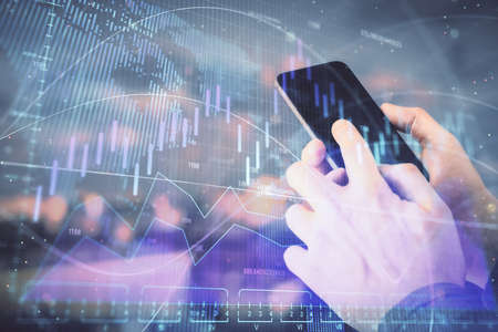 Double exposure of mans hands holding and using a digital device and forex graph drawing. Financial...