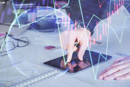 Double exposure of mans hands holding and using a digital device and forex graph drawing. Financial...