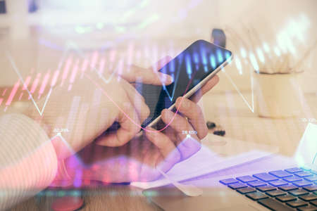 Double exposure of mans hands holding and using a digital device and forex graph drawing. Financial...