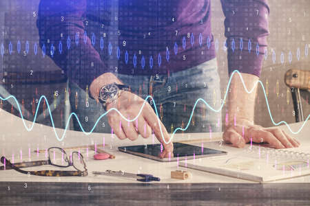 Double exposure of mans hands holding and using a digital device and forex graph drawing. Financial...