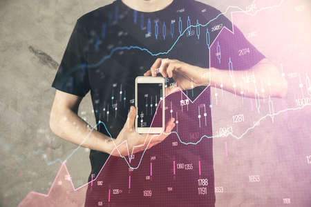 Double exposure of mans hands holding and using a digital device and forex graph drawing. Financial...
