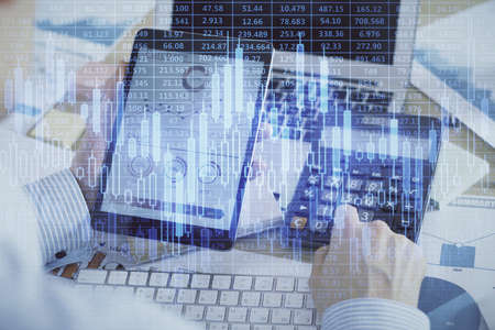 Double exposure of mans hands holding and using a digital device and forex graph drawing. Financial...