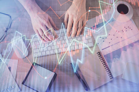 Multi exposure of mans hands typing over computer keyboard and forex graph hologram drawing. Top...