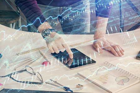 Double exposure of mans hands holding and using a digital device and forex graph drawing. Financial...