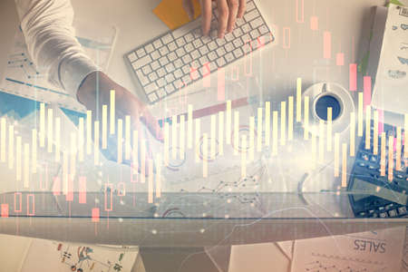 Multi exposure of mans hands typing over computer keyboard and forex graph hologram drawing. Top...