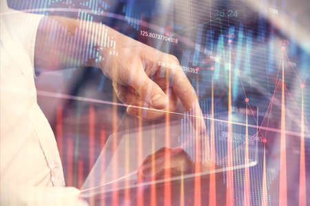 Double exposure of mans hands holding and using a digital device and forex graph drawing. Financial...