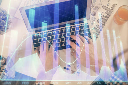 Double exposure of mans hands typing over laptop keyboard and forex chart hologram drawing. Top...
