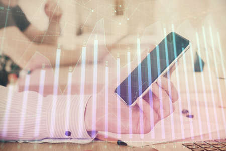 Double exposure of mans hands holding and using a digital device and forex graph drawing. Financial market concept.の写真素材